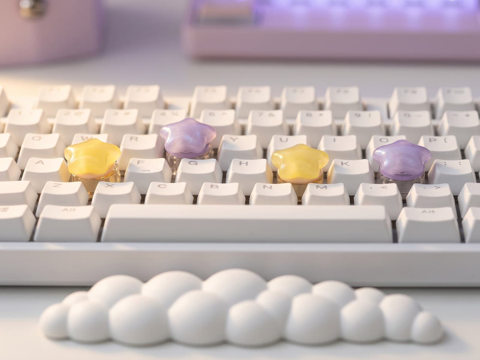 Macro close-up of Starry Glow yellow and Sparkle Star lavender artisan keycaps on a white mechanical keyboard, with a Dreamy Cloud Bubble wrist rest in the foreground